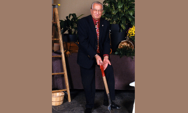 Mayor Bogs holds a shovel against a background of plants and garden implements. 