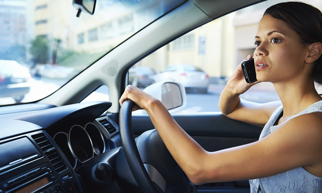 A young woman operates a vehicle while talking on a cell phone.