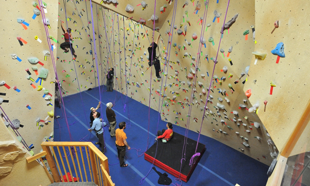 Indoor climbing walls with several climbers on the walls and several waiting
