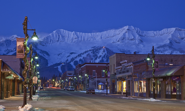 Downtown streetscape at night, with snow-covered mountains in the background