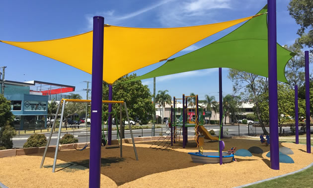 A yellow shade and a green shade are shading a playground with swings and a slide.