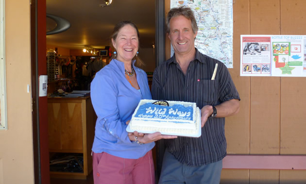 Happy-looking middle-aged couple stand just outside a building, holding a celebration cake.