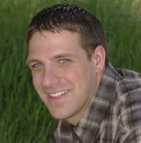 A head shot of Dylan Zorn wearing a brown plaid shirt against a field of green.