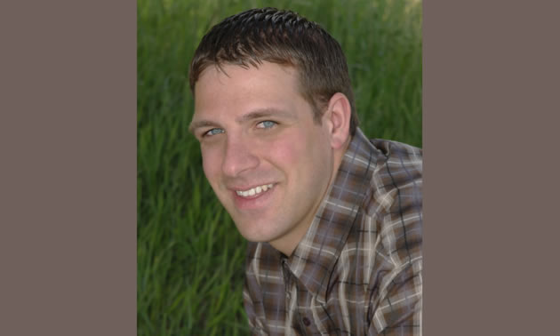 A head shot of Dylan Zorn wearing a brown plaid shirt against a field of green.
