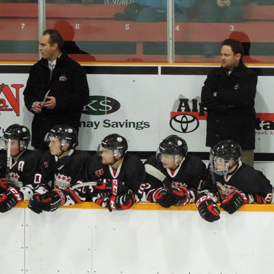 Kimberley Dynamiters head coach Derek Stuart stands with two other coaches behind the bench at a Kimberley Dynamiters hockey game