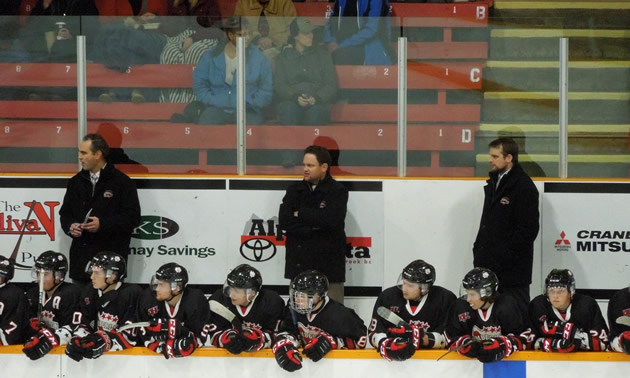 Kimberley Dynamiters head coach Derek Stuart stands with two other coaches behind the bench at a Kimberley Dynamiters hockey game