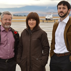 Two men and one woman stand on an airport runway on a grey day.
