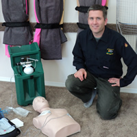 Mike kneels alongside stretchers mounted on the wall. Beside him is medical training equipment such as a CPR dummy.