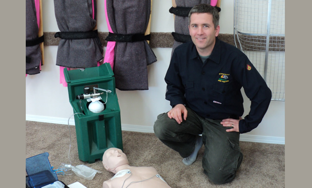 Mike kneels alongside stretchers mounted on the wall. Beside him is medical training equipment such as a CPR dummy.