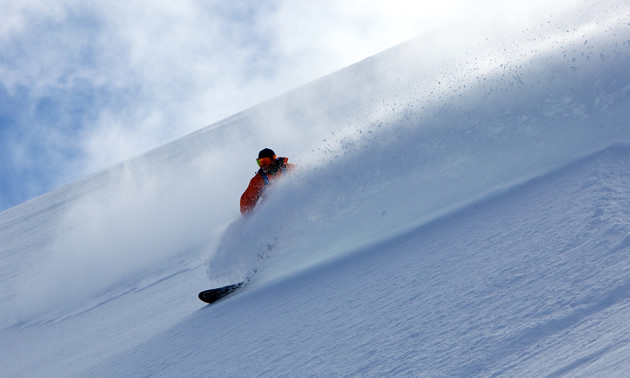 A slope of blowing snow is interrupted by a figure on a snowboard in a cloud of snow.