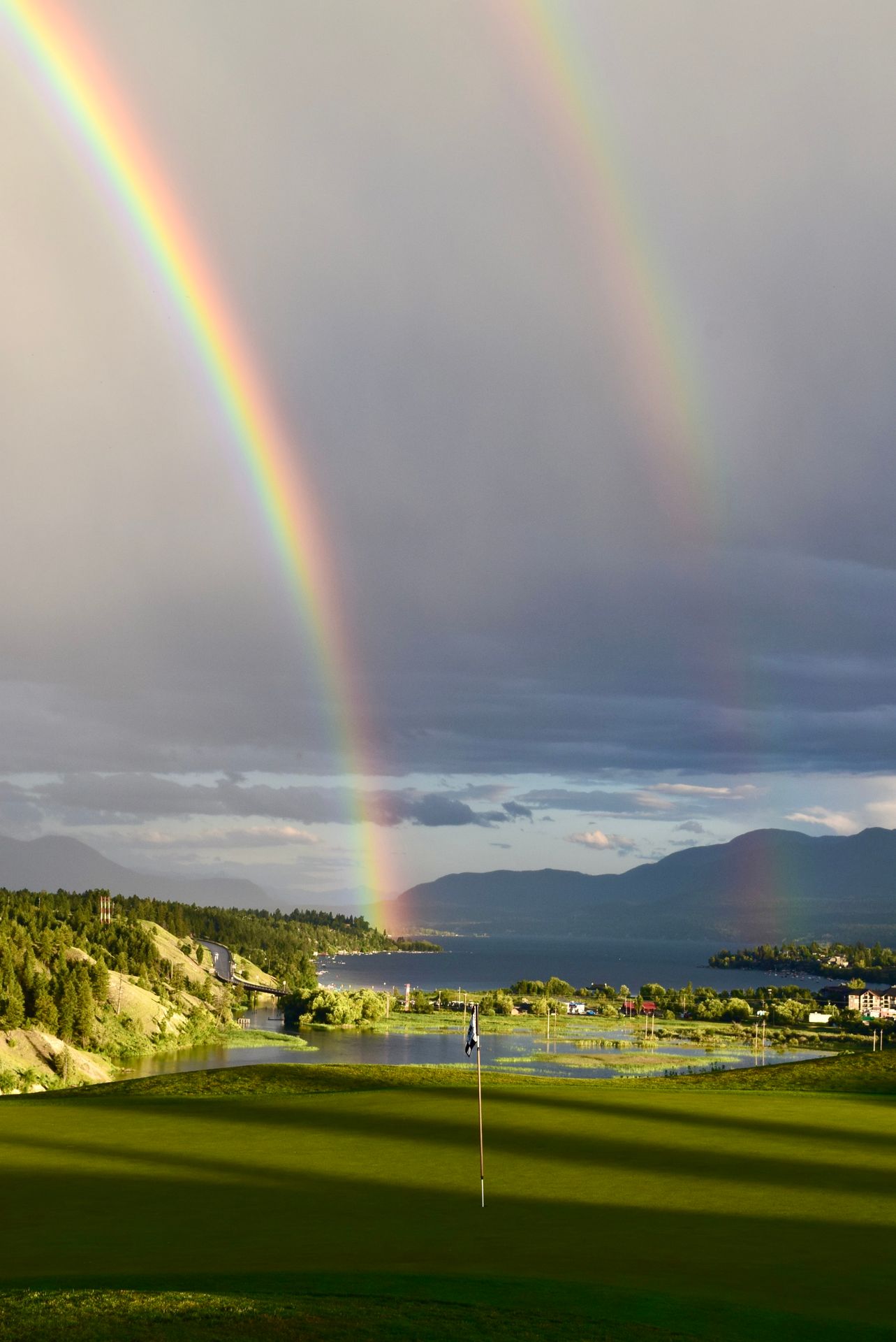 Panoramic view of distant mountains, lake, rainbow. 