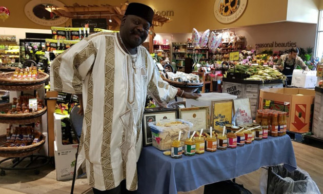 Owner of Ebesse Zozo Hot Sauce with display of products in grocery store. 