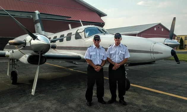 Two pilots stand in front of a small aircraft owned by ELT Aviation, based in Cranbrook, B.C.