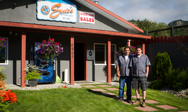 Two men stand on the lawn in front of an attractive building that reads 