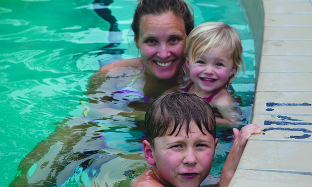 A smiling woman with two small children together in a swimming pool