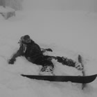 Young woman wearing ski apparel lies laughing in the snow.