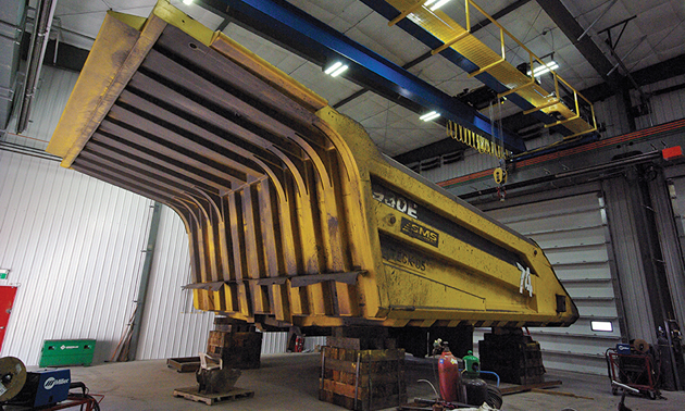 A large piece of metal equipment sits on wood beam supports inside a workshop