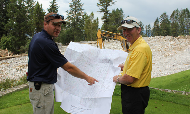 Two men examine landscape drawings; golf course in the background