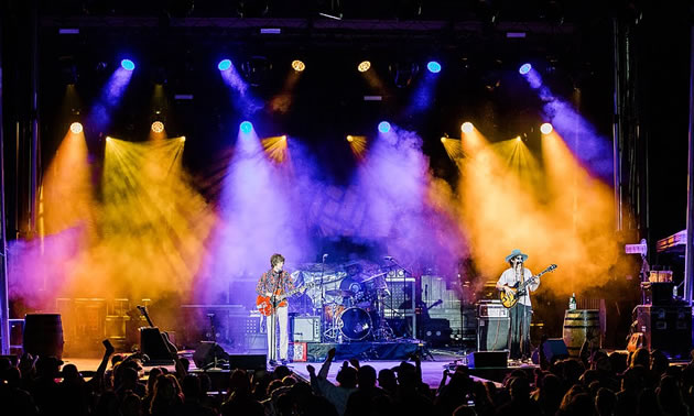 Performers on stage at FarmJam 2019 - nighttime shot, stage lit up with purple and yellow lights. 