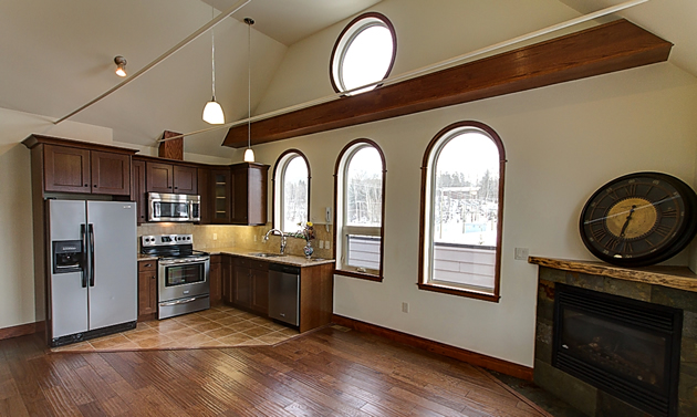 An open room with three domed windows, a corner kitchen and a fireplace.