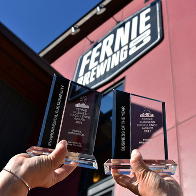 Person holding up two awards in front of Fernie Brewing Co. sign. 