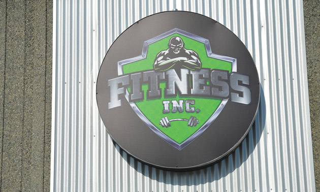 Round sign in green on metallic grey, with the words Fitness Inc. 