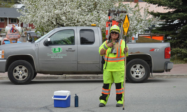 Female flag person, Theresa Clarke, in high-visibility gear, with a D&B Flagging truck behind her