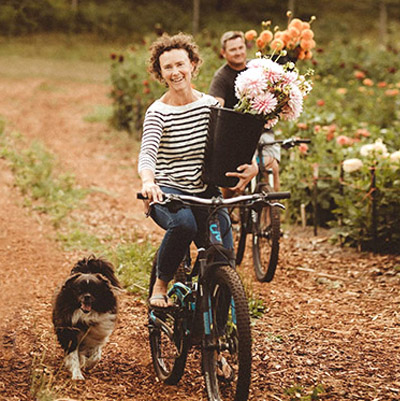Owners of Stone Meadows Gardens riding bikes and carrying flowers. 