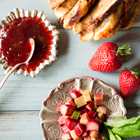A display of sliced baked pastry, small dishes holding red jam and diced  rhubarb, and fresh strawberries.