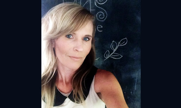 Carmen Adams smiles for the camera against a chalkboard and writing.