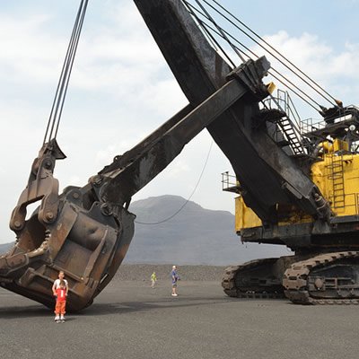 A man and child are dwarfed by the giant mining machine that is parked beside them.
