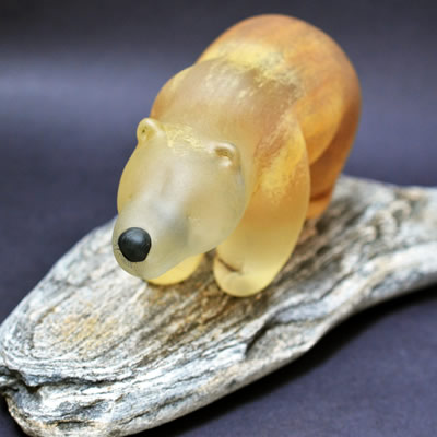 An ivory-coloured glass bear is standing on a piece of wood.