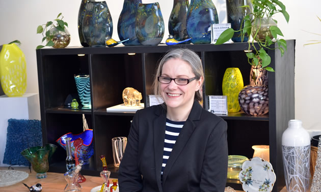 Diana Fox is standing in front of display shelves of glass items.