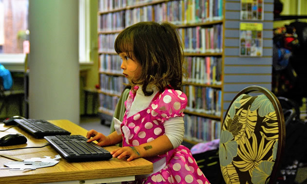 Little girl dressed in pink using a computer. 