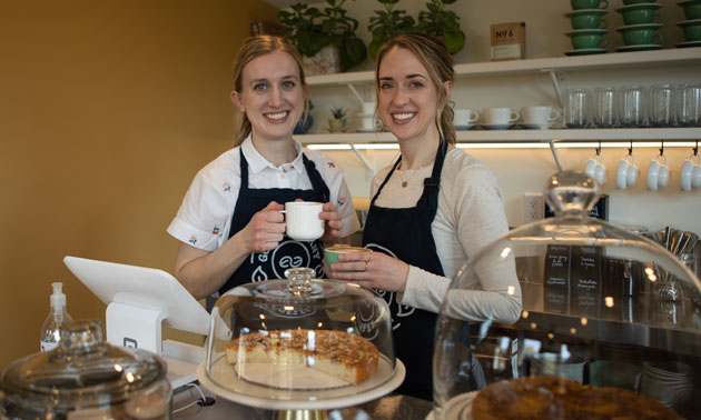 Sisters Stephanie and Cassidy Tilling posing behind display of baked goods. 