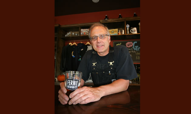 A man with glasses sitting with a beer in a mug