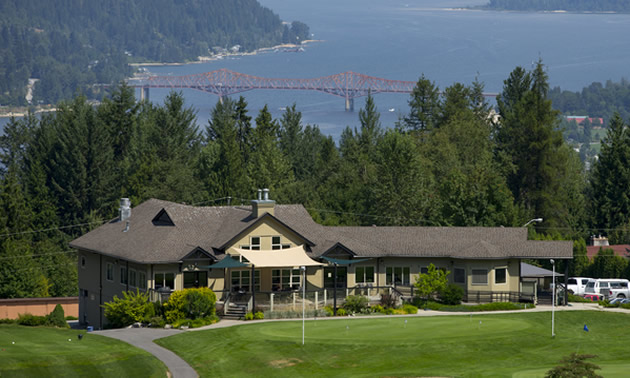 View of golf club house on hill, with lake in background. 