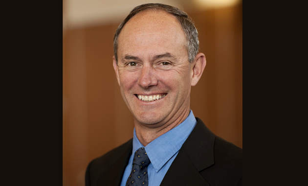 A headshot of Grant Sharam. He wears a suit and tie while smiling.