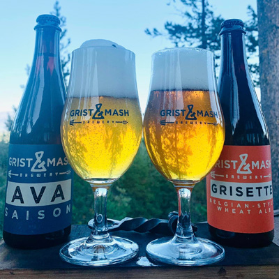 Two frosty glasses of beer in middle of photo, with two bottles of Grist and Mash beer on either side of glasses. 