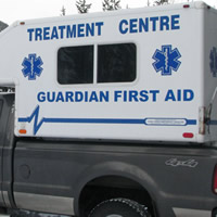 A woman standing beside a black pickup truck carrying a white camper with a sign saying Treatment Centre Guardian First Aid