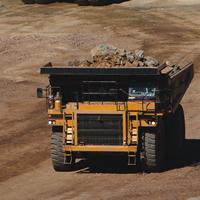 A number of haul trucks and other heavy machinery operate in a dull brown pit.