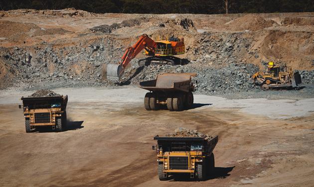 A number of haul trucks and other heavy machinery operate in a dull brown pit.
