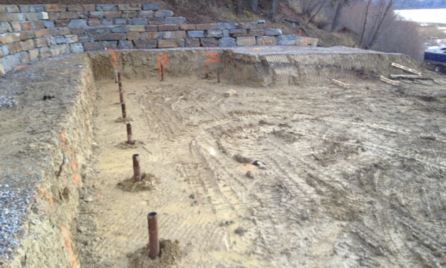 A row of implanted helical piles in a shallow excavation, apparently a foundation site