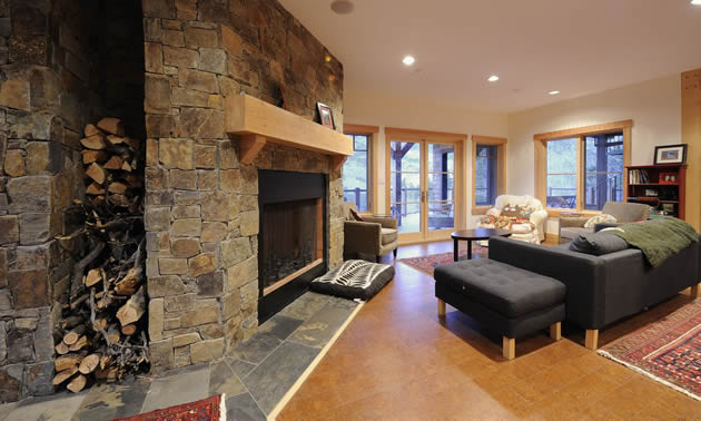 Living room with wood floors, a large stone fireplace and floor-to-ceiling windows