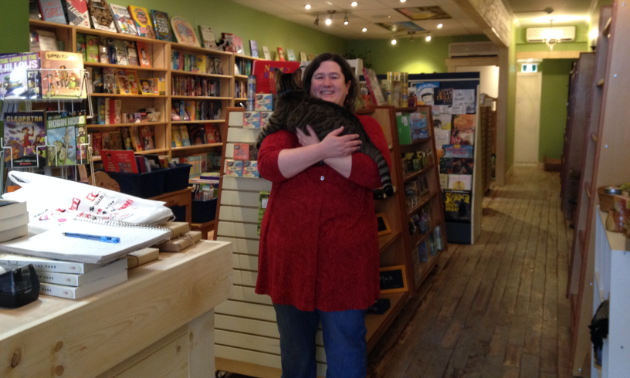 Owner of Huckleberry Books, Erin Dalton, standing in bookstore with Max the cat cuddled in her arms. 