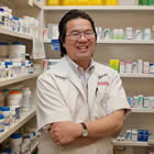 Steven Hui, wearing a lab coat, helps a customer from behind the counter at his Pharmasave store.