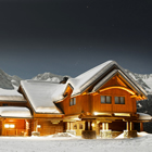 Log timber ski lodge, capped with snow, with mountain background