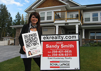 Photo of Sandy Smith standing by a house holding up a QR code sign