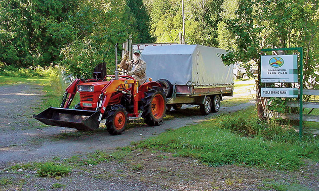 Bent Haagerup drives a big red tractor with a trailer at Tesla Springs Farm
