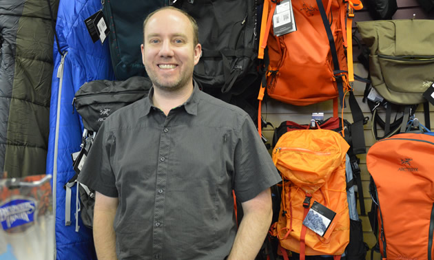 Smiling man standing in front of a wall display of backpacks